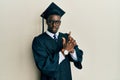 Handsome black man wearing graduation cap and ceremony robe holding symbolic gun with hand gesture, playing killing shooting Royalty Free Stock Photo