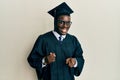 Handsome black man wearing graduation cap and ceremony robe pointing fingers to camera with happy and funny face Royalty Free Stock Photo