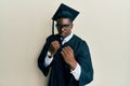 Handsome black man wearing graduation cap and ceremony robe ready to fight with fist defense gesture, angry and upset face, afraid