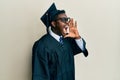 Handsome black man wearing graduation cap and ceremony robe shouting and screaming loud to side with hand on mouth Royalty Free Stock Photo