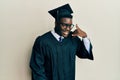 Handsome black man wearing graduation cap and ceremony robe smiling doing phone gesture with hand and fingers like talking on the Royalty Free Stock Photo