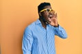 Handsome black man wearing yellow glasses shouting and screaming loud to side with hand on mouth Royalty Free Stock Photo