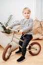 Handsome blond boy sitting on a small beige two wheel bike inside a room