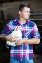 Handsome blond farmer holding a white chicken