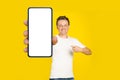 Handsome blond man pointing at giant smartphone with white empty screen, wearing white t-shirt and jeans cellphone Royalty Free Stock Photo