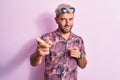 Handsome blond man on vacation wearing casual shirt and sunglasses over pink background pointing fingers to camera with happy and Royalty Free Stock Photo