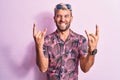 Handsome blond man on vacation wearing casual shirt and sunglasses over pink background shouting with crazy expression doing rock Royalty Free Stock Photo