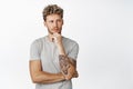 Handsome blond tattooed man, looking away with thoughtful face, thinking, standing in gray t-shirt over white background Royalty Free Stock Photo