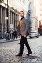 Handsome blonde man walking on city street wearing a smart casual outfit with a jacket and black pants in New York City SoHo distr