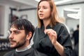 Handsome blue eyed man sitting in barber shop. Hairstylist Hairdresser Woman cutting his hair. Female barber Royalty Free Stock Photo