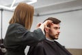 Handsome blue eyed man sitting in barber shop. Hairstylist Hairdresser Woman cutting his hair. Female barber Royalty Free Stock Photo