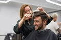 Handsome blue eyed man sitting in barber shop. Hairstylist Hairdresser Woman cutting his hair. Female barber Royalty Free Stock Photo