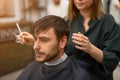 Handsome blue eyed man sitting in barber shop. Hairstylist Hairdresser Woman cutting his hair. Female barber Royalty Free Stock Photo