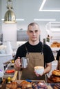 Handsome bold male baker posing with coffee and cream jug in hands