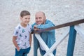 Handsome bold stylish dressed in jeans man in blue cap sitting on a beach sea side together with cute son boy teen andpretty engli