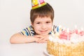 A handsome boy celebrates a birthday, sits in front of a cake with candles and makes a wish