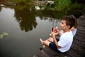 Handsome boy eating watermelon, enjoying beautiful summer day at sunset, sitting on the pier with his feet submerged in the lake,
