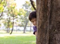 Handsome boy hiding behind tree for playing hide and seek with friend at park or son hiding mother behind tree because little kid Royalty Free Stock Photo