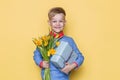 Handsome boy holding flower bunch and gift box. Valentine`s day. Birthday. Mother`s day. Studio portrait over yellow background Royalty Free Stock Photo