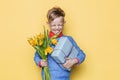 Handsome boy holding flower bunch and gift box. Valentine`s day. Birthday. Mother`s day. Studio portrait over yellow background Royalty Free Stock Photo