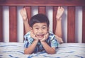 Handsome boy lying barefoot on bed in bedroom. Happy child smiling. Vintage tone effect.