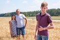 Handsome boy portrait with his father and preteen sister on background, Caucasian family in wheat field