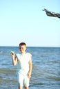 Handsome boy in shorts and a t-shirt teenager launches a kite on the sky on the seashore