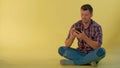 Handsome boy sitting on the floor and chatting with friends on smartphone