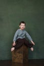 Handsome boy sitting on  wooden box, bewildered look, emotions of surprise on his face, squeezing and playing Royalty Free Stock Photo