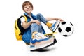 Handsome boy sitting on yellow skateboard and holding leg on soccer ball on white background. Back to School. Royalty Free Stock Photo
