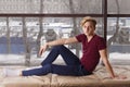 Handsome boy teenager in t-shirt sits on soft windowsill