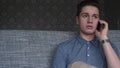 Handsome boy teenager talking on the phone sits on a gray sofa Royalty Free Stock Photo