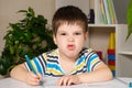 A handsome boy of 4 years old learns to write, looks into the camera and grimaces.
