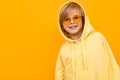 Handsome boy in yellow hoodie smiles and gesticulates isolated on orange background