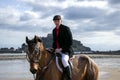 Good Looking Male Horse Rider Riding Horse On Beach In Traditional Riding Clothing With St Michael`s Mount In Background