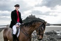 Handsome Male Horse Rider riding horse on beach in traditional fashion with St Michael`s Mount in background Royalty Free Stock Photo
