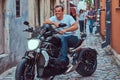 A handsome brutal biker, ride on a motorcycle, in a narrow old Europe street.