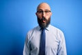 Handsome business bald man with beard wearing elegant tie and glasses over blue background afraid and shocked with surprise Royalty Free Stock Photo