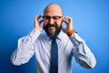 Handsome business bald man with beard wearing elegant tie and glasses over blue background covering ears with fingers with annoyed