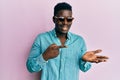 Handsome business black man wearing stylish sunglasses amazed and smiling to the camera while presenting with hand and pointing Royalty Free Stock Photo