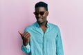 Handsome business black man wearing stylish sunglasses smiling with happy face looking and pointing to the side with thumb up Royalty Free Stock Photo