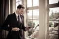 Handsome business executive standing next to hotel window using his mobile cellphone device