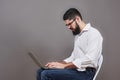 Handsome business man in glasses and suit holding laptop in hands and writing something. Side view. Isolated gray Royalty Free Stock Photo