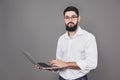 Handsome business man in glasses and suit holding laptop in hands and writing something. Side view. Isolated gray Royalty Free Stock Photo