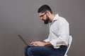 Handsome business man in glasses and suit holding laptop in hands and writing something. Side view. Isolated gray Royalty Free Stock Photo