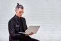 Handsome business man in glasses and suit holding laptop in hands and writing something. Side view. On white brick Royalty Free Stock Photo