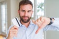 Handsome business man holding credit card with angry face, negative sign showing dislike with thumbs down, rejection concept Royalty Free Stock Photo