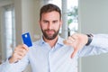 Handsome business man holding credit card with angry face, negative sign showing dislike with thumbs down, rejection concept Royalty Free Stock Photo