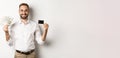 Handsome business man showing credit card and money dollars, smiling satisfied, standing over white background Royalty Free Stock Photo