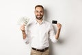 Handsome business man showing credit card and money dollars, smiling satisfied, standing over white background Royalty Free Stock Photo